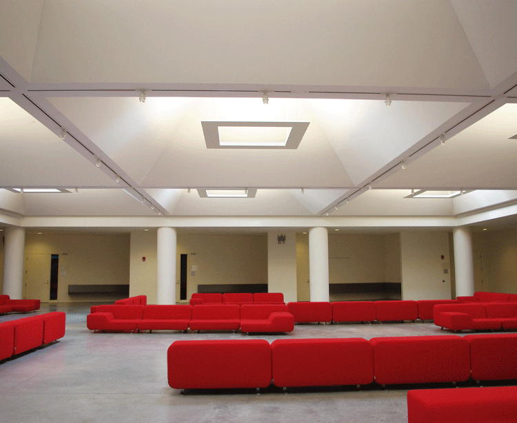 basement interior with white grid ceiling, columns, floor and red lounge chairs