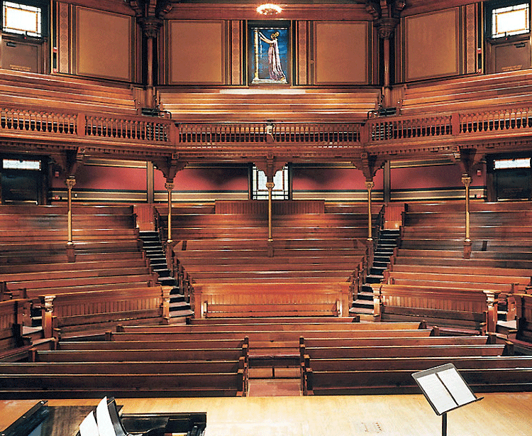 interior view of the semicircular wooden mezzanine and orchestra in Sanders Theatre, with a grand piano and music stand on stage